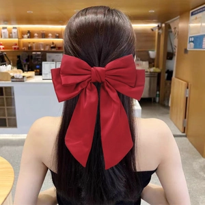 Elegant red bow hair clip with long ribbons shown on a model in a cozy cafe setting