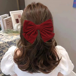 Detail view of a large burgundy velvet bow hair clip worn on dark wavy hair in retro style
