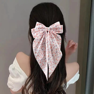 Close-up of a large cream bow hair clip with red heart patterns on long wavy hair