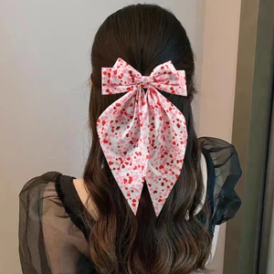 Pink bow hair clip with red heart prints and long ribbons shown on a model's hair