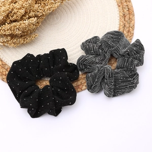 Détail de deux chouchous noirs à paillettes avec texture brillante sur un tapis tissé