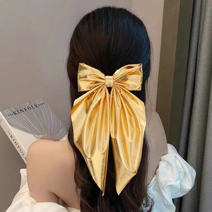 Elegant gold metallic bow hair clip with long ribbons styled on long wavy hair