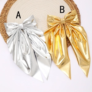 Elegant metallic bow hair clip with long ribbons in gold and silver colors on a woven mat
