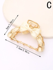 Detailed view of golden metal hair claw with cream satin bow and hollow chain pattern
