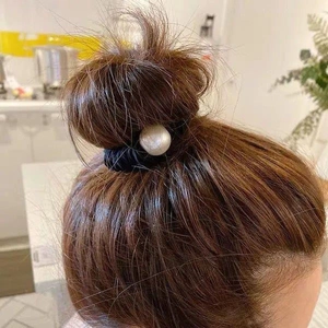Detail showing a black scrunchie with white pearl accessory on a messy bun hairstyle