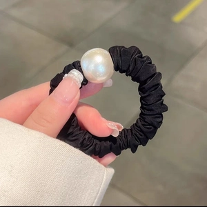 Close-up of a black scrunchie with a large white pearl bead being held by hand