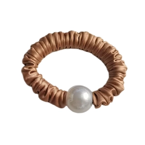 Close-up of champagne gold satin scrunchie featuring a large pearl and pleated texture
