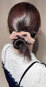 Detailed texture of the striped orange and beige knit scrunchie on a bun hairstyle