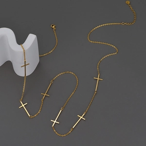 Minimalistische goldene Edelstahlkette mit Kreuzanhängern auf grauem Grund