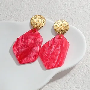 Detail of pink marble acrylic earrings with sunflower embossed gold studs on stone tray