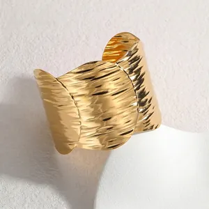 Exaggerated wide gold cuff bracelet with hammered texture and wavy edges on white stand