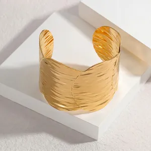 Minimalist wide gold open cuff bracelet with hammered wavy texture on white platform