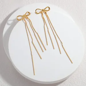 Detailed close-up of golden bow earrings with long metallic fringe tassels on a display