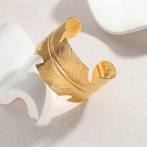 Polished gold feather open cuff bracelet with detailed texture on minimalist display
