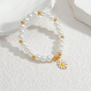 Dettaglio del bracciale con ciondolo a margherita, perle bianche e sfere dorate su sfondo