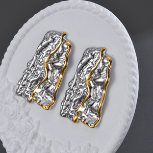 Irregular textured gold and silver square earrings on a white floral embossed plate