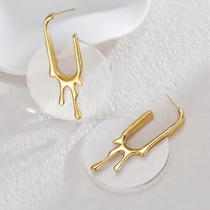 Détail de boucles d'oreilles en U dorées avec texture lave sur fond texturé blanc