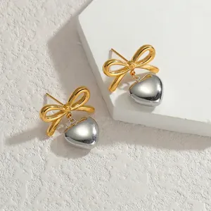 Vue détaillée de boucles d'oreilles nœud doré avec pendentifs cœur argenté sur pierre