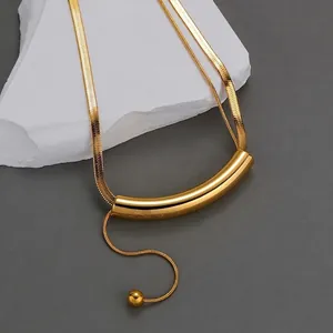 Minimalist gold stainless steel tube tassel necklace on white textured stone background