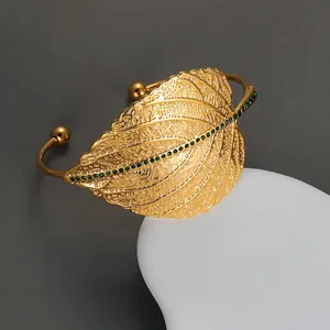 Detail of vintage gold-plated open bangle featuring green rhinestones on leaf veins