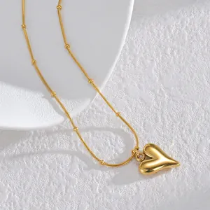 Polished gold heart pendant necklace with beaded snake chain on white texture