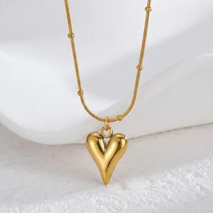 Polished gold heart pendant necklace with beaded snake chain on a minimalist display