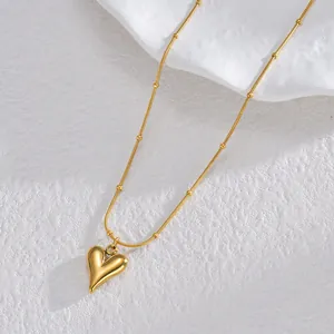 Fashionable golden heart pendant necklace with snake chain on white stone display