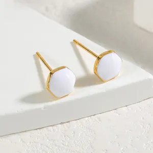 Macro view of geometric hexagonal gold stud earrings with white enamel inlay on stone