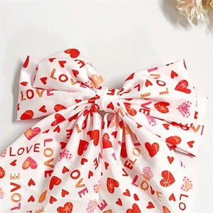 Detail of white satin bow hair clip with red heart patterns and LOVE lettering