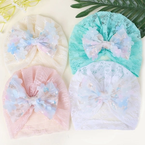 Détail de bonnets en dentelle pour bébé avec grands nœuds à paillettes et fleurs en 3D