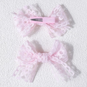 Détail des barrettes à nœud en dentelle rose montrant la broderie fine et la pince crocodile