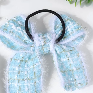 Détail de l'élastique à cheveux avec nœud en tweed bleu clair, bordure fourrure et fils d'or