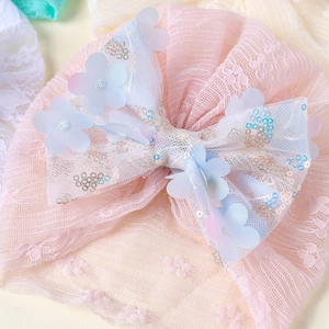Détail d'un turban en dentelle rose pour bébé avec un grand nœud à paillettes et fleurs