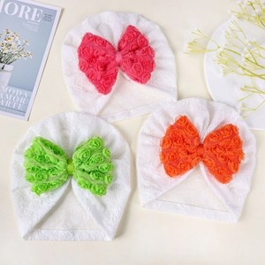 Dettaglio di tre cappelli neonato in maglia con fiocchi di rose 3D in chiffon colorato