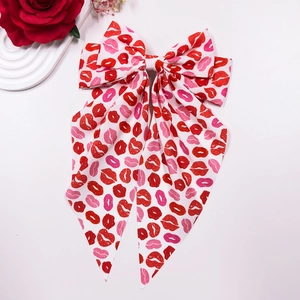 Detail of oversized bow hair clip featuring red lip prints and long elegant ribbons