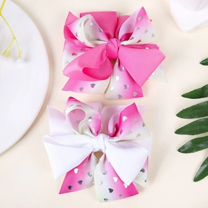 Detail of gradient pink ribbon hair clips with shiny silver heart patterns and ribbed texture