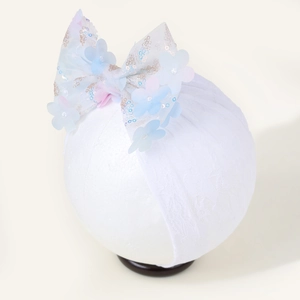 Détail d'un bandeau bébé en dentelle avec grand nœud en résille et fleurs pailletées