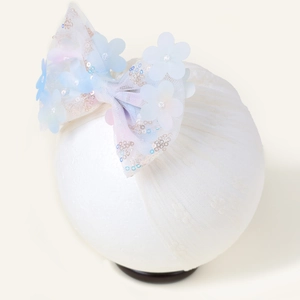 Détail d'un bandeau pour bébé en dentelle blanche avec un nœud à paillettes et pétales