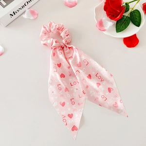 Détail du chouchou en satin rose avec imprimé LOVE rouge et cœurs sur table blanche