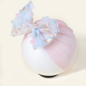 Détail du bandeau bébé en maille rose avec grand nœud fleuri à paillettes sur modèle