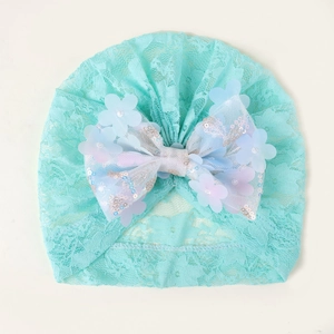Détail du bonnet en dentelle vert menthe pour bébé avec grand nœud à paillettes et fleurs