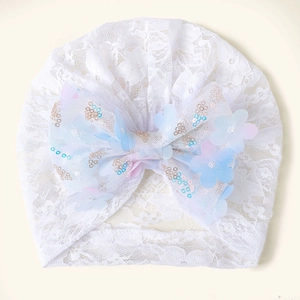 Détail d'un bonnet de bébé en dentelle blanche avec nœud pailleté et fleurs dégradées