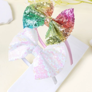 Dettaglio di cerchietti con fiocchi di paillettes arcobaleno e bianche per bambina