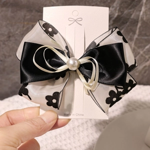 Détail d'un nœud papillon multicouche en satin noir et ruban floral avec perle centrale