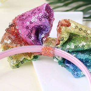 Dettaglio di cerchietto con fiocco di paillettes arcobaleno e raso rosa per bambine
