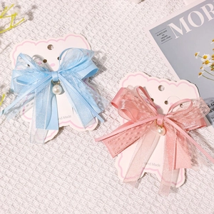Close-up of lace bow hair clips with hanging pearls and ribbons on display card