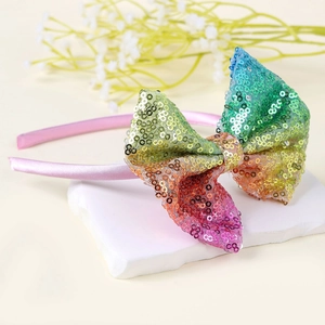 Dettaglio del cerchietto con fiocco di paillettes arcobaleno su raso rosa per bimbi