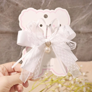 Detailed view of white lace ribbon hair clip with pearl pendant on a pink card