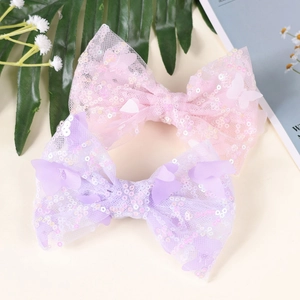 Detailed view of pink and purple sequin bow hair clips on a soft beige background
