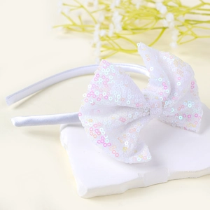 Dettaglio di paillettes lucide su un cerchietto con fiocco in raso bianco per bambine